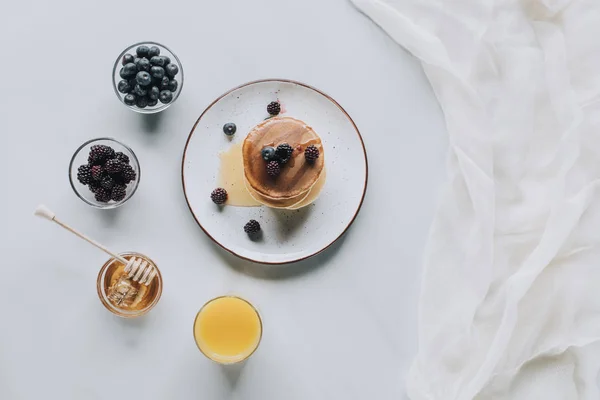 Vista dall'alto di dolci frittelle saporite con miele, bacche e succo su grigio — Foto stock