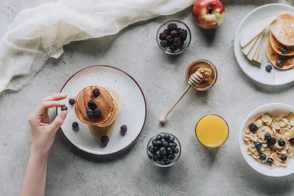 Partial top view of person eating delicious homemade pancakes with honey and fruits on grey — Stock Photo