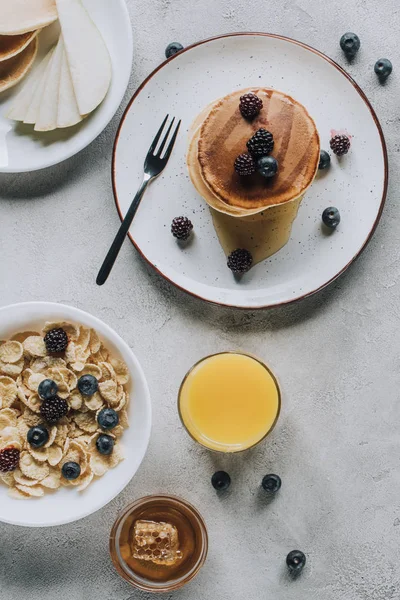 Blick von oben auf leckere hausgemachte Pfannkuchen, Glas Saft, Honig und Müsli auf grau — Stockfoto