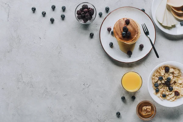 Vista superior de delicioso desayuno casero con panqueques, frutas, miel y muesli en gris - foto de stock
