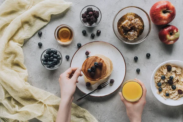 Vista superior parcial de la persona que toma un desayuno saludable con panqueques caseros, frutas frescas y miel en gris - foto de stock