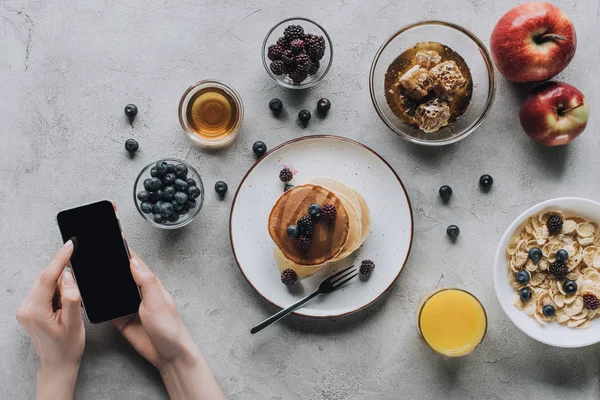 Обрізаний знімок людини, використовуючи смартфон, маючи здоровий смачний сніданок — стокове фото