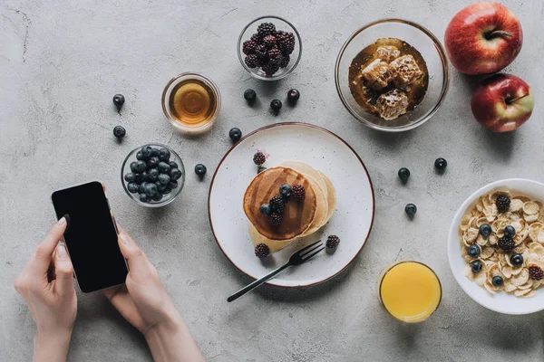 Tiro recortado de la persona que usa el teléfono inteligente mientras desayuna sabroso saludable - foto de stock