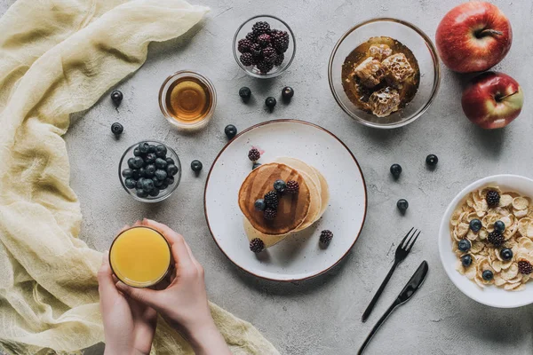 Blick von oben auf Person, die gesundes Frühstück mit hausgemachten Pfannkuchen, frischem Obst und Honig auf grau isst — Stockfoto