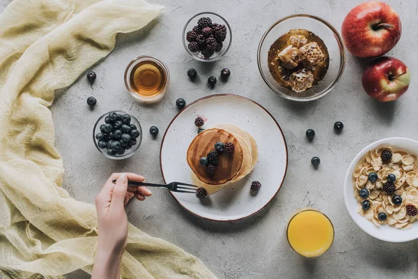 Cropped shot of person eating healthy breakfast with homemade pancakes, fresh fruits and honey on grey — Stock Photo