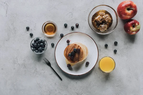 Vista dall'alto di dolci frittelle fatte in casa con bacche fresche e miele su grigio — Foto stock