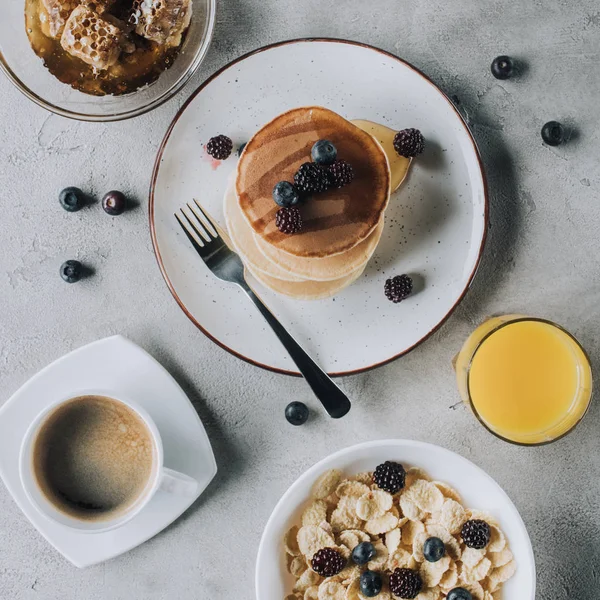 Süße Pfannkuchen mit Beeren, Saft, Honig, Müsli und Kaffee auf grau — Stockfoto