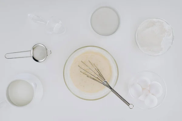 Vista superior de la masa y batidor, ingredientes y utensilios para cocinar panqueques aislados en gris - foto de stock