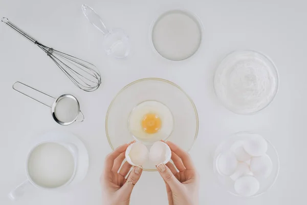 Tiro recortado de la persona sosteniendo cáscara de huevo mientras cocina panqueques aislados en gris - foto de stock