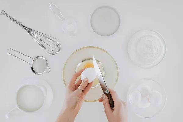 Tiro recortado de la persona sosteniendo huevo y cuchillo mientras que cocina panqueques aislados en gris - foto de stock