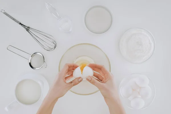 Tiro recortado de la persona sosteniendo huevo mientras cocina panqueques aislados en gris - foto de stock