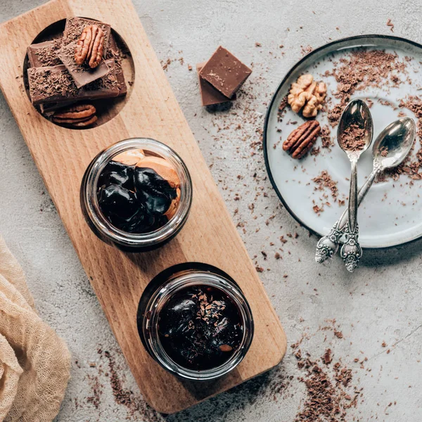 Top view of sweet homemade desserts in glass jars and chocolate pieces  with nuts — Stock Photo