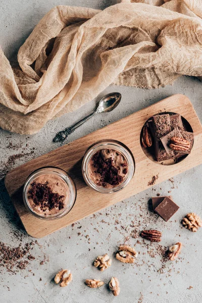 Vista superior de dulces postres caseros en frascos de vidrio y trozos de chocolate sobre tabla de madera — Stock Photo