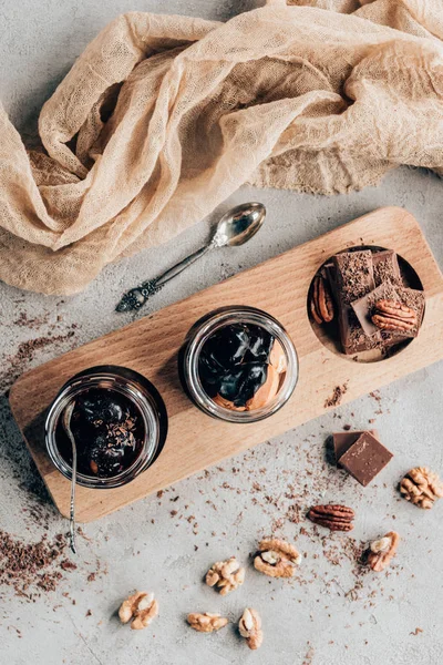 Vista superior de sobremesas doces em frascos de vidro e pedaços de chocolate na placa de madeira — Fotografia de Stock