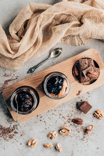 Vista superior de postres dulces en frascos de vidrio y trozos de chocolate sobre tabla de madera - foto de stock