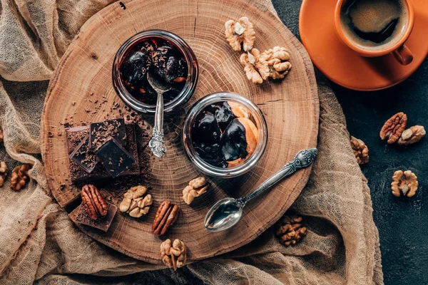 Vista dall'alto di deliziosi dessert in barattoli di vetro e pezzi di cioccolato con noci e tazza di caffè — Foto stock