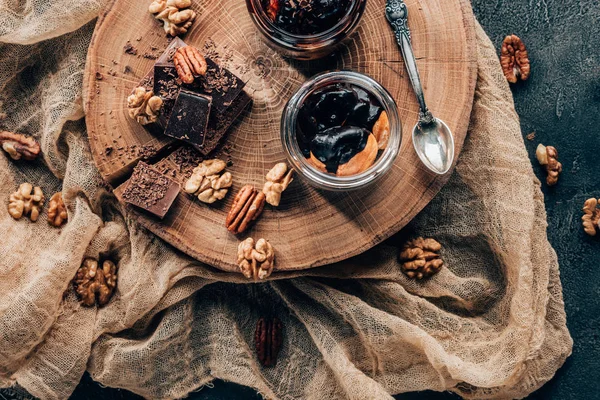 Vue du dessus de délicieux desserts dans des bocaux en verre et des morceaux de chocolat avec des noix sur un plateau en bois — Photo de stock