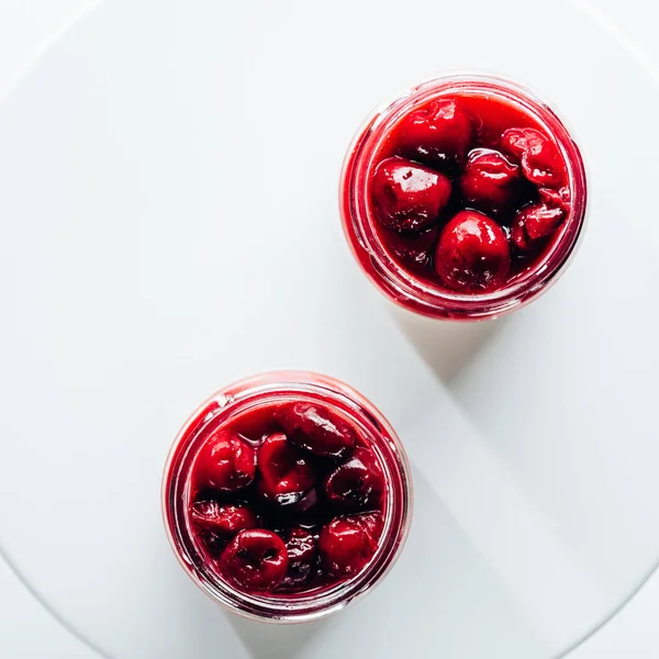 Вид зверху солодкого здорового вишневого десерту в скляних банках на білому — стокове фото