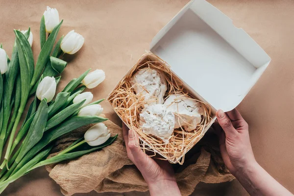 Plan recadré de la personne tenant boîte avec de délicieux biscuits meringués et des tulipes blanches — Photo de stock