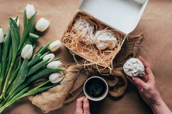 Plan recadré de la personne buvant du café et mangeant des biscuits près des tulipes blanches — Photo de stock