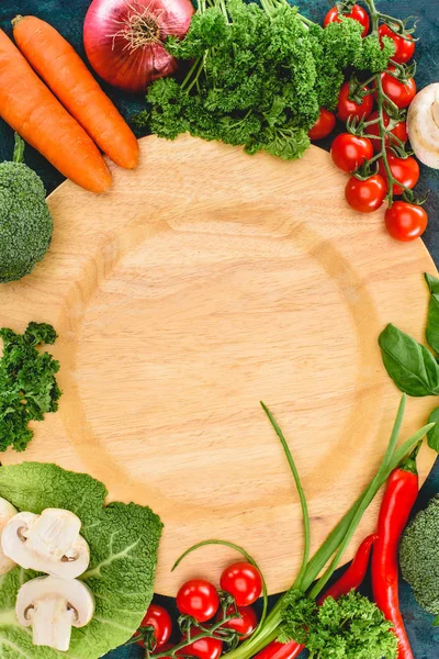 Vista superior de verduras crudas frescas y saludables y plato de madera vacío — Stock Photo