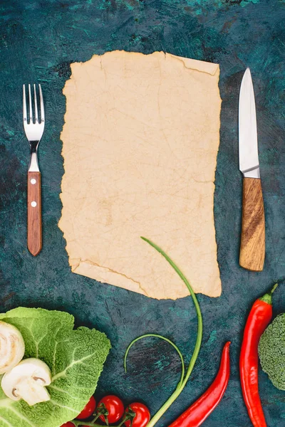 Vista superior de pergaminho em branco, garfo com faca e vegetais crus em preto — Fotografia de Stock