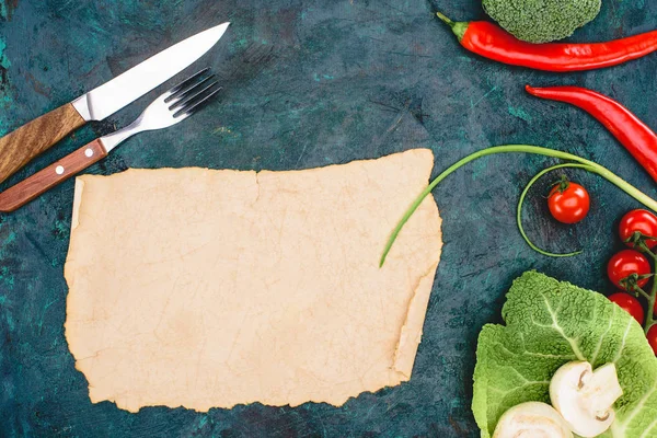 Top view of blank parchment, fork with knife and ripe raw vegetables on black — Stock Photo