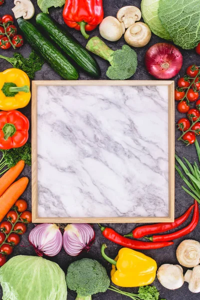 Vue du dessus de légumes crus frais et panneau de marbre blanc sur noir — Photo de stock