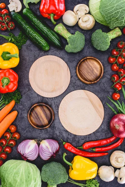 Top view of empty wooden plates and fresh raw organic vegetables on black — Stock Photo