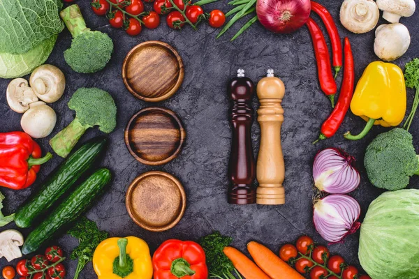 Top view of fresh organic vegetables, wooden plates and containers for spices on black — Stock Photo