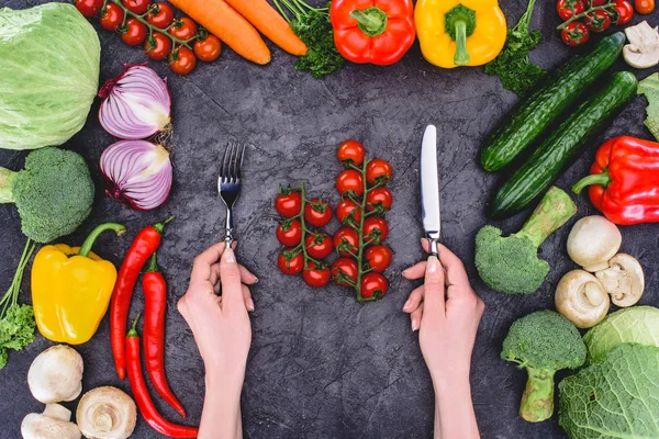 Tiro recortado de la persona sosteniendo tenedor y cuchillo sobre verduras frescas saludables en negro - foto de stock