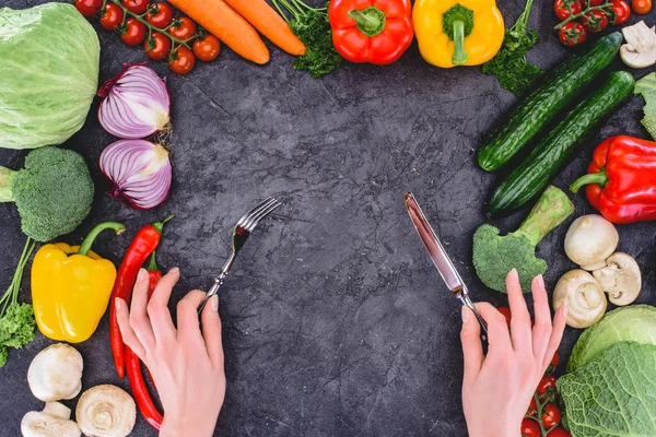 Cropped shot of hands holding fork and knife above healthy fresh vegetables on black — Stock Photo