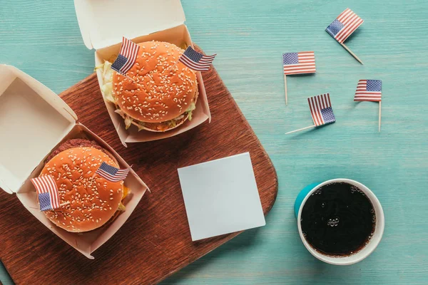 Vista superior de hamburguesas arregladas y refrescos con banderas americanas en la mesa de madera, concepto de celebración del día de los presidentes - foto de stock