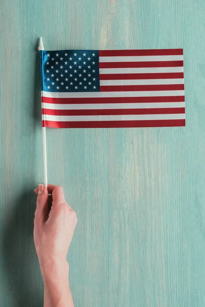 Partial view of woman holding american flag in hand on blue wooden tabletop, presidents day concept — Stock Photo