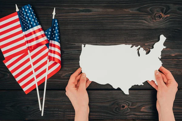Vista superior de bandeiras americanas dispostas e mãos femininas com pedaço de mapa em branco na mesa de madeira, conceito do dia dos presidentes — Fotografia de Stock