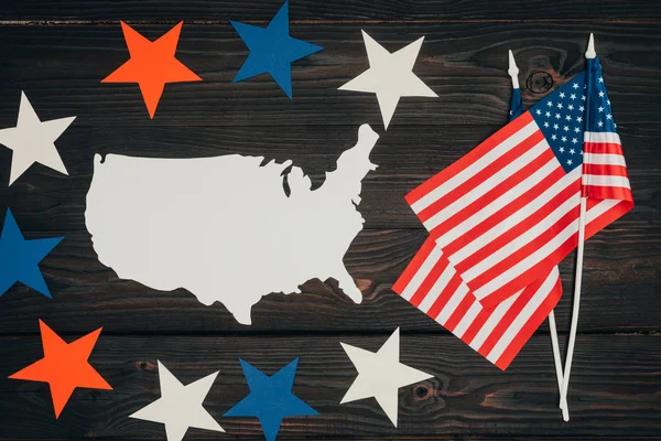 Vista superior de bandeiras americanas dispostas, pedaço de mapa feito de papel e estrelas na superfície de madeira, conceito de celebração do dia dos presidentes — Fotografia de Stock
