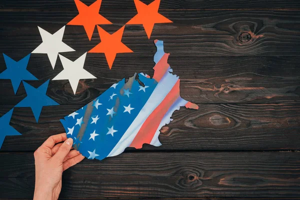 Tiro recortado de estrelas e mão feminina com pedaço de mapa com bandeira americana na mesa de madeira, conceito dia presidentes — Fotografia de Stock