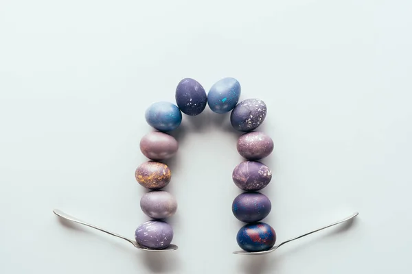Vista superior de la composición con huevos de Pascua morados y azules en cucharas, aislados en blanco - foto de stock