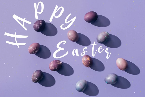 Painted chicken eggs on purple background with Happy Easter lettering — Stock Photo