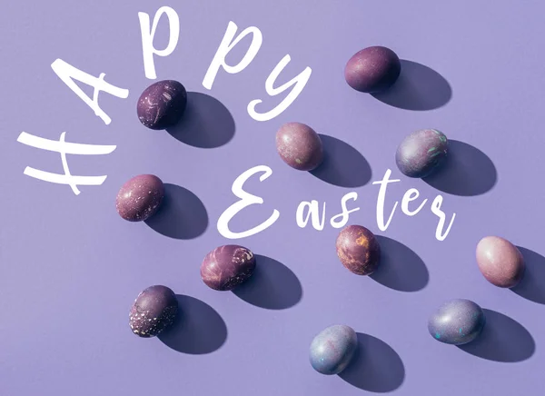 Painted chicken eggs on purple background with Happy Easter lettering — Stock Photo