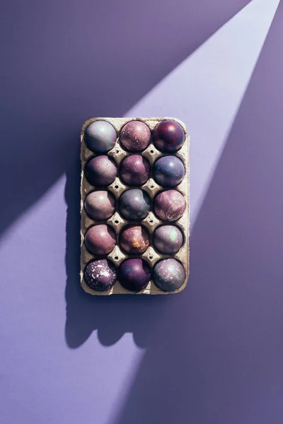 Oeufs violets de Pâques dans un grand plateau sur fond violet avec rayon de soleil — Photo de stock