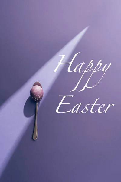 Painted egg in spoon on purple background with Happy Easter lettering — Stock Photo