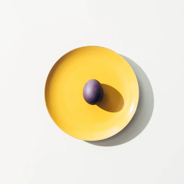 Top view of purple easter egg on yellow plate, on white — Stock Photo