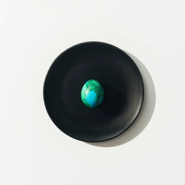 Top view of blue and green easter egg on black plate, on white — Stock Photo