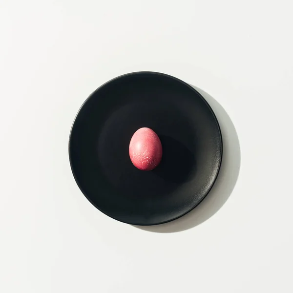 Vista dall'alto di uovo di Pasqua rosso su piatto nero, su bianco — Foto stock