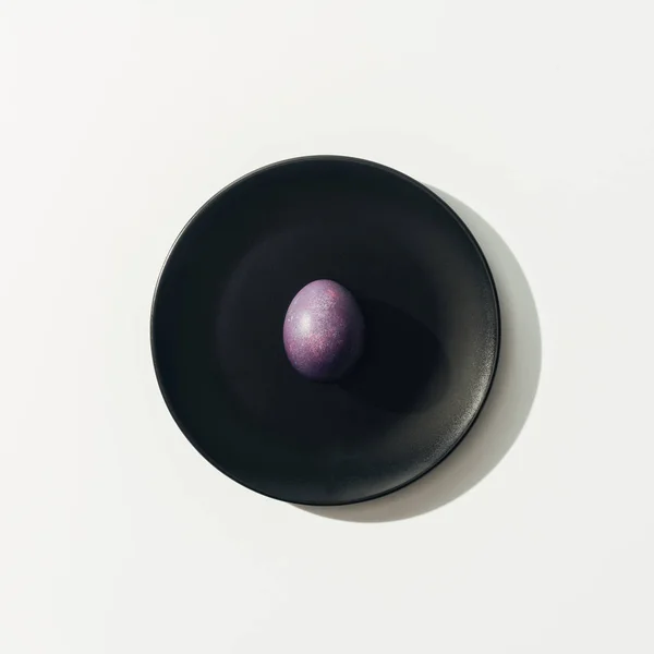 Top view of purple easter egg on black plate, on white — Stock Photo