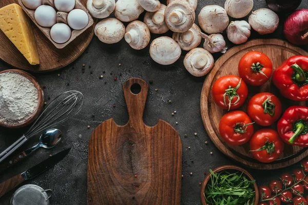 Vista superior de diferentes ingredientes crudos para pizza y tabla de cortar en superficie de hormigón — Stock Photo