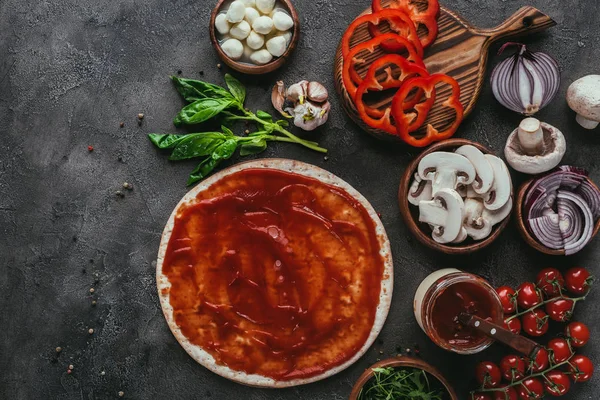 Vue du dessus de la pâte à pizza crue avec sauce et légumes sur table en béton — Photo de stock