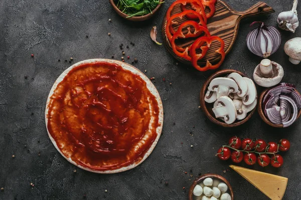 Vista superior de la masa de pizza con ketchup y verduras en la mesa de hormigón — Stock Photo