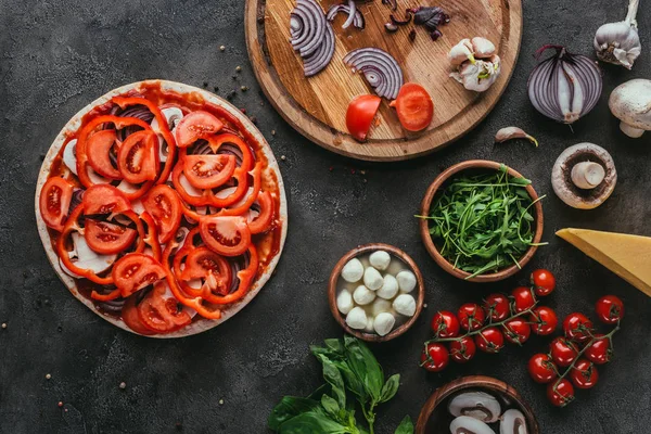 Vista superior de la pizza cruda con diferentes ingredientes en la mesa de hormigón - foto de stock
